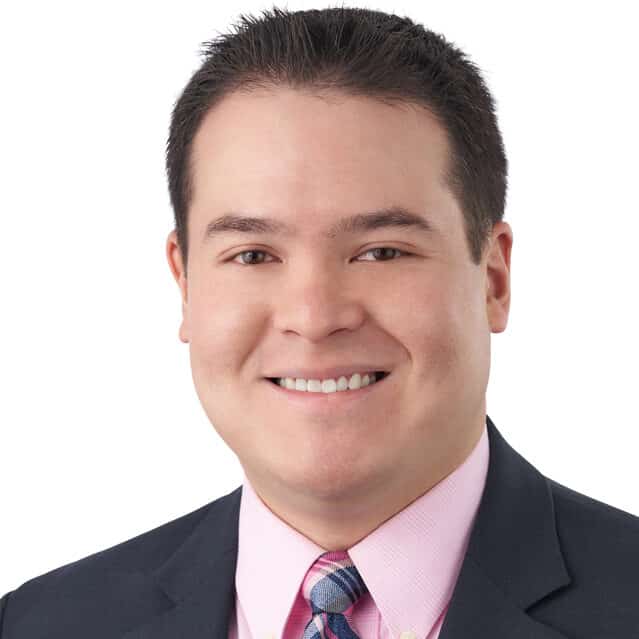 A headshot of associate Erik Hickman. He has short black hair and he is wearing a black suit.