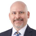 A headshot of associate Garrett Spangler. He is smiling at the camera and waring a navy blue suit.