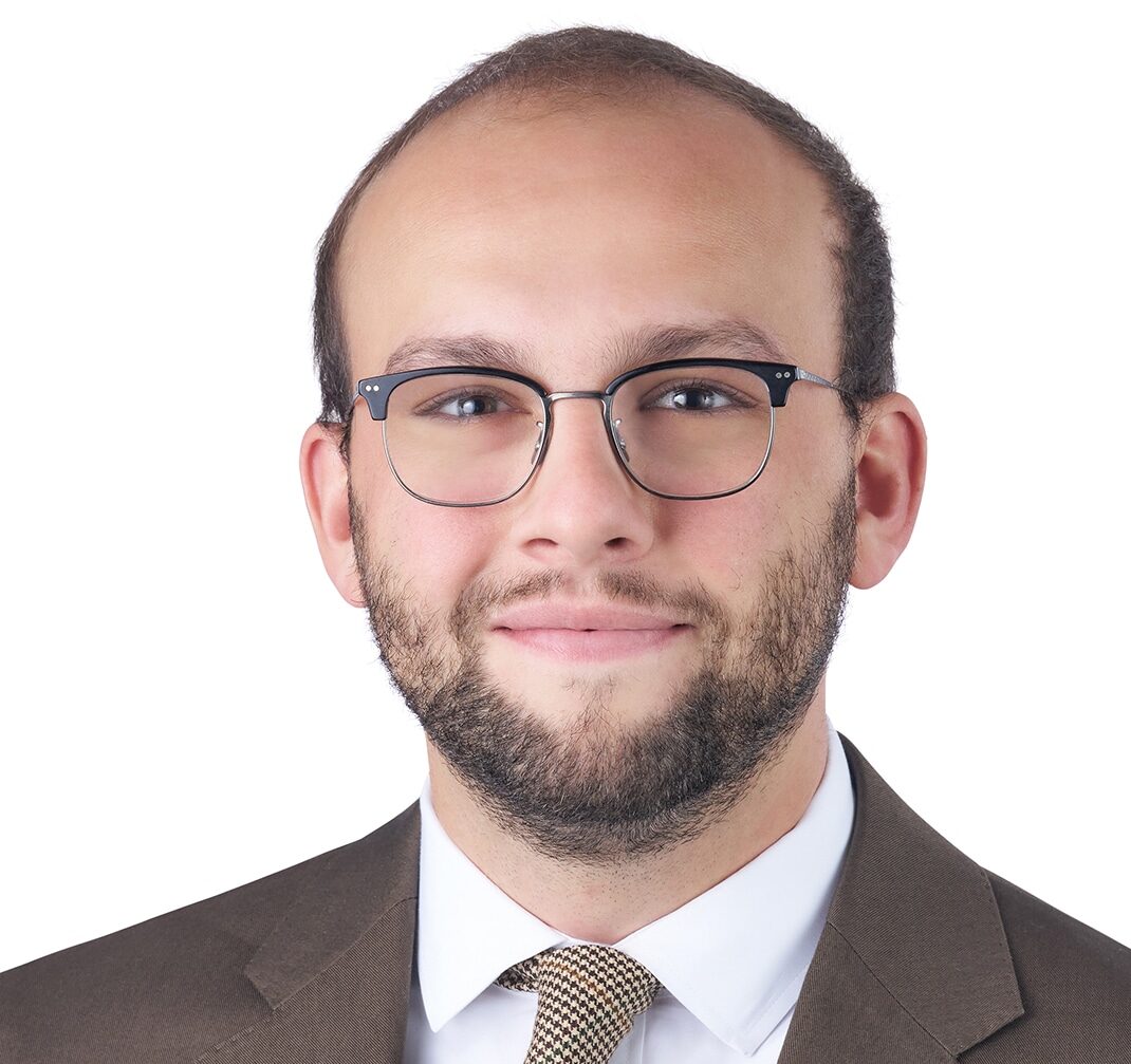 A headshot of associate Cade Reed. He is wearing black browline eyeglasses and a brown suit.