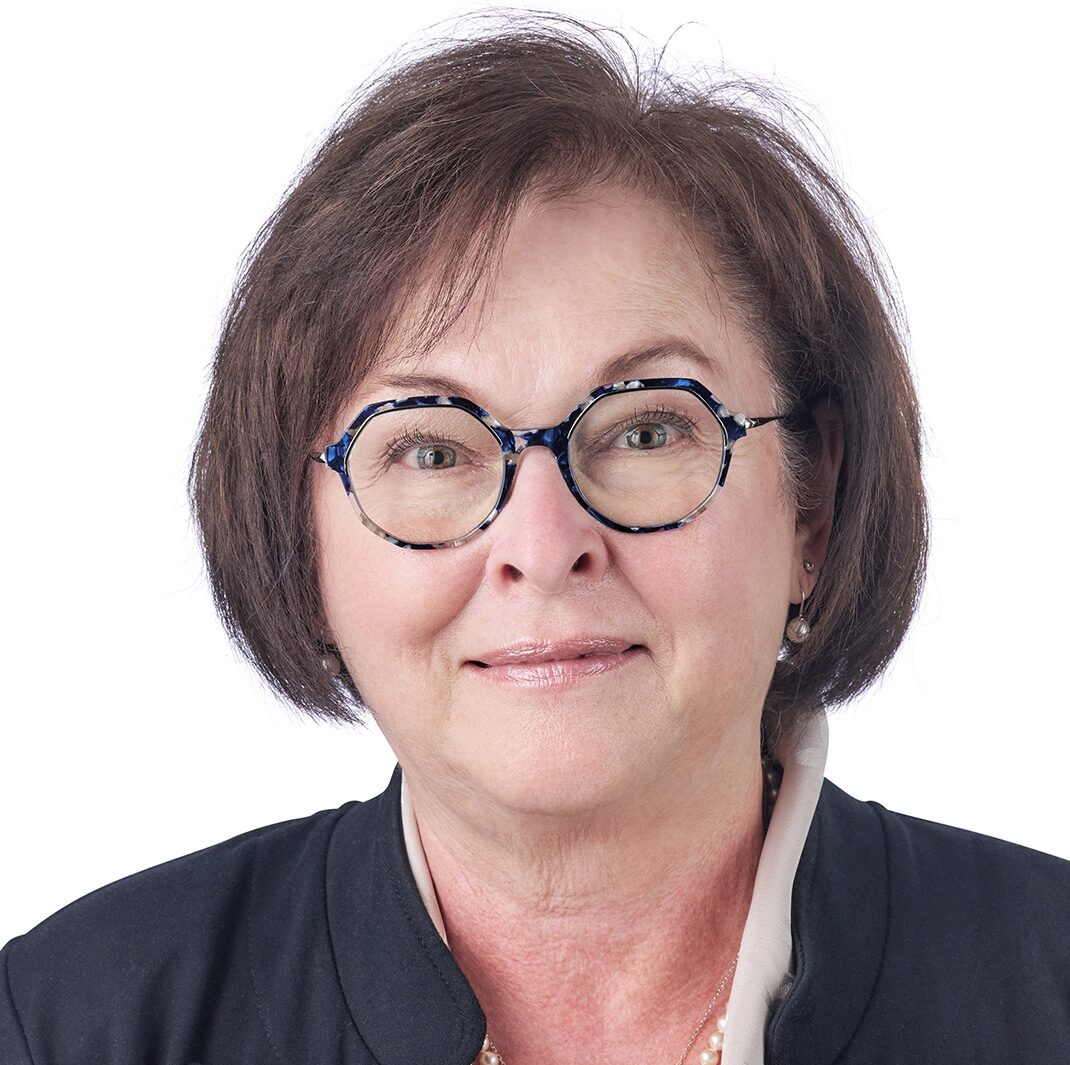A headshot of associate Sally Lawson. She has short brown hair, multi-colored eyeglasses, and she is wearing a black blazer.